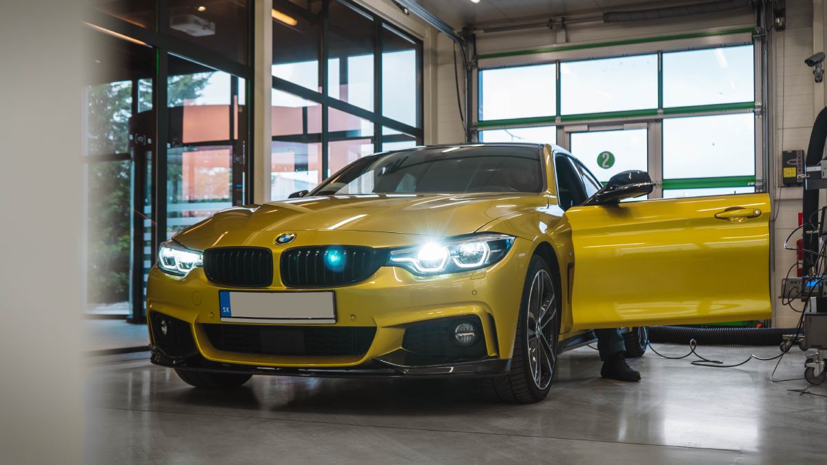 Žlté športové auto BMW zaparkované v interiéri servisnej haly BigaSTK, pripravené na úpravy alebo detailing.